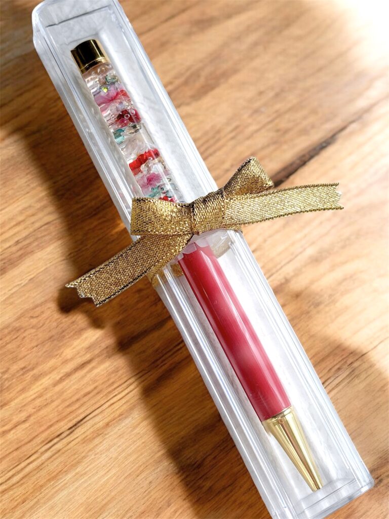 「赤いボールペンとハーバリウム部分を組み合わせたギフトセット。ゴールドリボン付きケースに入った贈り物仕様。」