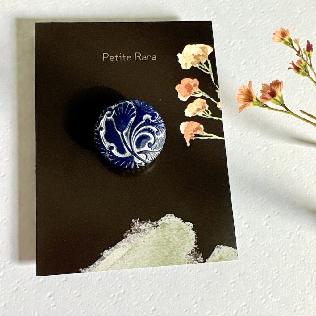 Petite Raraオリジナル台紙にセットされた藍色×白のチェコガラス帯留め「蒼華 -Souka-」。花のイラストが添えられた展示イメージ写真。