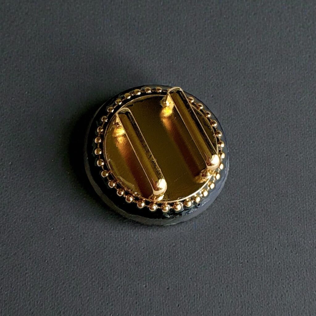 チェコガラス帯留め「蒼華 -Souka-」の裏面金具。ゴールドの帯留め金具が黒背景で輝くディテール写真。