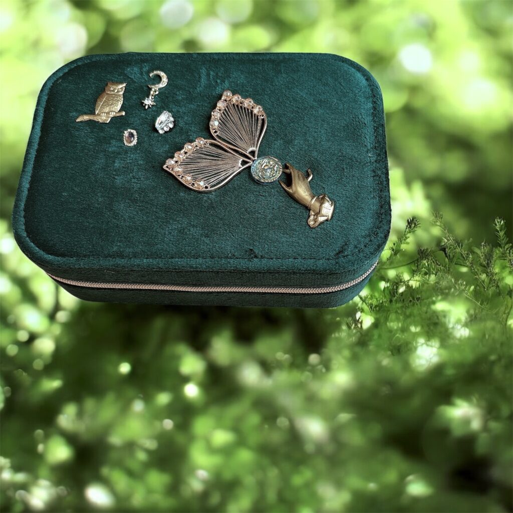 深緑のフェアリーチャーム付きジュエリーケースが、柔らかな光の差し込む森の背景に置かれた幻想的なイメージ