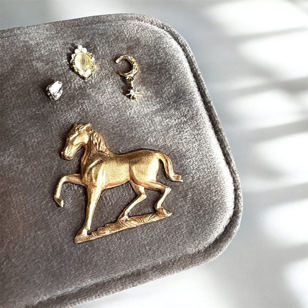 アースグレーのジュエリーケースに飾られたゴールドの馬と、淡い光を放つ月と星のチャーム。冬の光に照らされた Fairy Realm Collection のディテール
