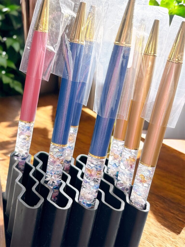 「ブルー・ピンク・ブラウン軸のハーバリウムボールペンが並ぶ。色とりどりの花材が輝く多色展開のペンコレクション。」