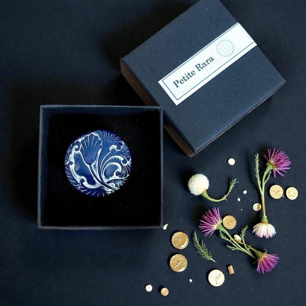 Petite Raraのギフトボックスと、藍色×白のチェコガラス帯留め「蒼華 -Souka-」。黒背景に小花と金色パーツが散る上品な商品イメージ写真。