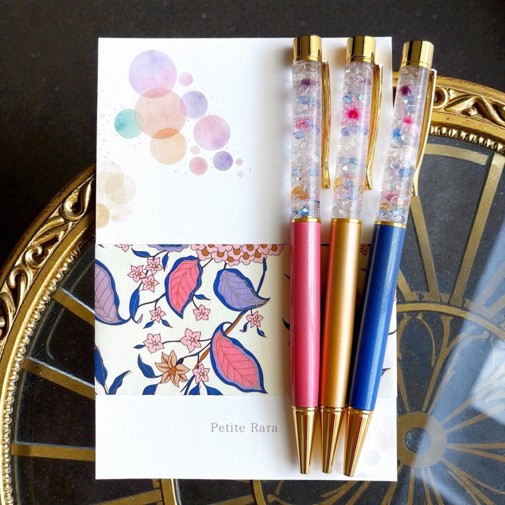 Moonlit Bloom｜淡い光が差す中、花の余韻を映した3本のハーバリウムボールペン。優しいブルーとピンク、ゴールドが夜明け前の静けさを思わせる配置。