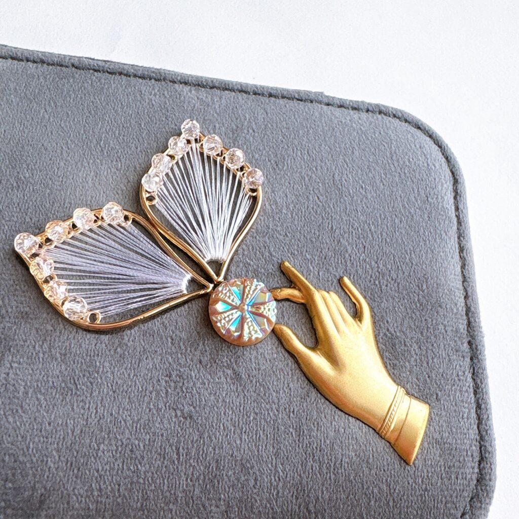 チェコガラスと糸を重ねた繊細な装飾と、そっと触れる仕草を表した手のモチーフをあしらったジュエリーケースの蓋装飾。Fairy Realm Collection作品。

Close-up of delicate Czech glass and thread ornament with a hand motif gently reaching toward it, from the Fairy Realm Collection.
