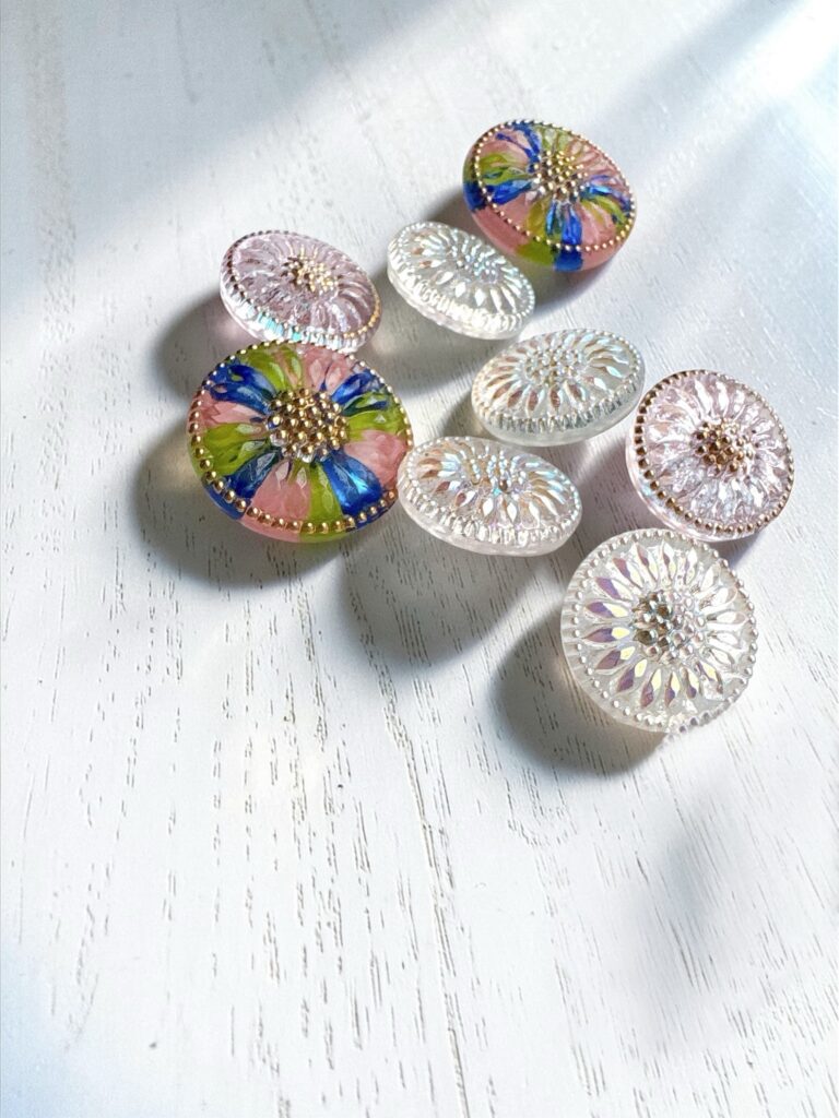 白い背景に並べられたチェコガラスのボタンやパーツ。やわらかな光の中で、それぞれ異なる色や模様が静かに輝いている。