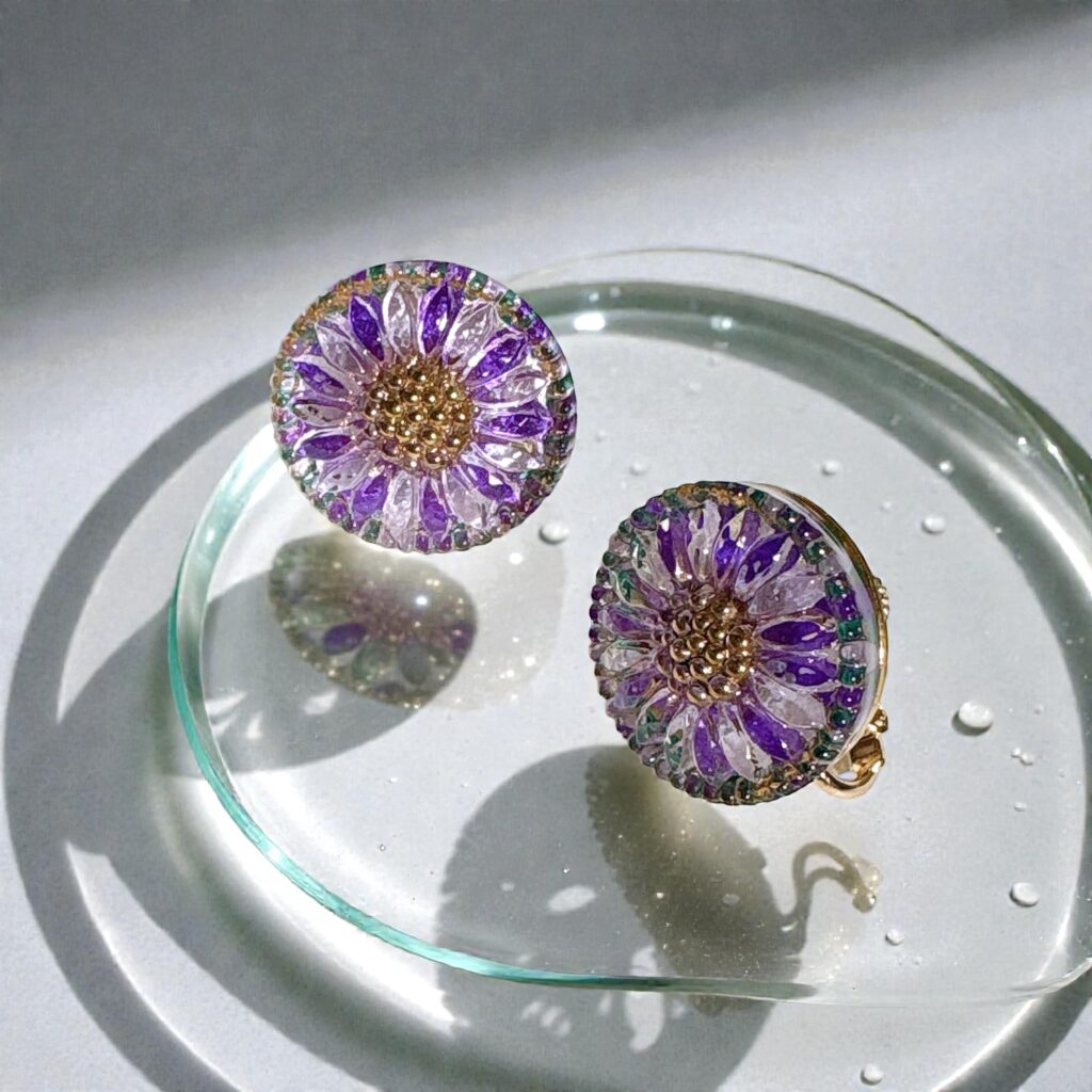 紫色の花模様が美しいチェコガラスイヤリング。光を受けて透明感と立体模様が浮かび上がり、水面のようなガラス皿の上で静かにきらめいている。