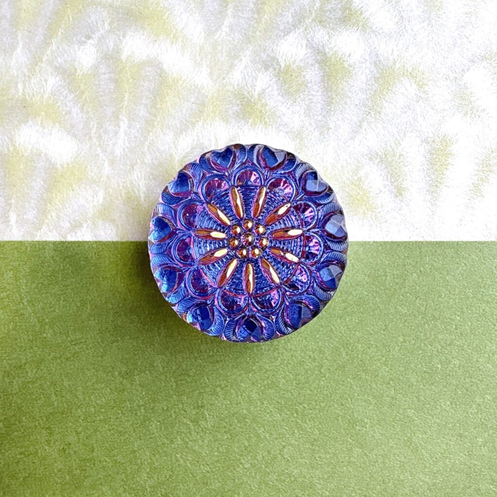 瑠璃色に輝く花模様のチェコガラス帯留。青や紫が重なり合う立体模様が、光を受けて繊細にきらめいている。