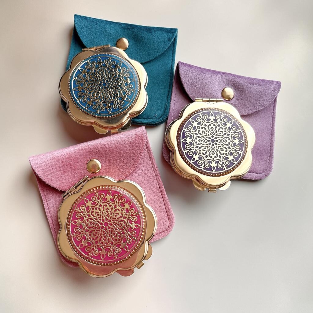 Bloom Mirror 3色展開。ローズピンク、ターコイズブルー、ラベンダーのコンパクトミラーと、それぞれに合わせた専用ケースを並べた商品写真。アンティーク調の透かし模様とゴールドカラーが上品な印象。